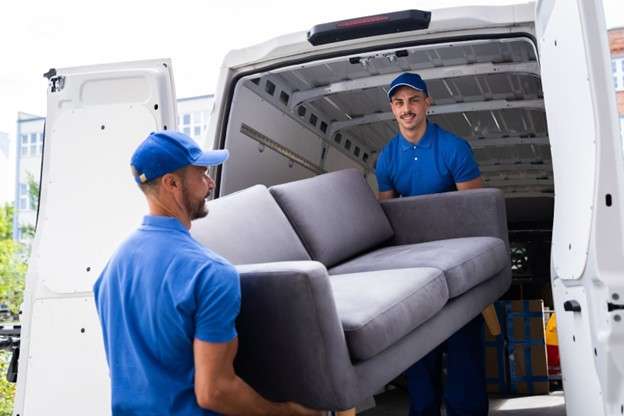 Two movers hauling a couch inside a moving truck
