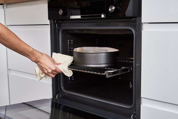 A hand pushing a rack with a pan inside the electric oven