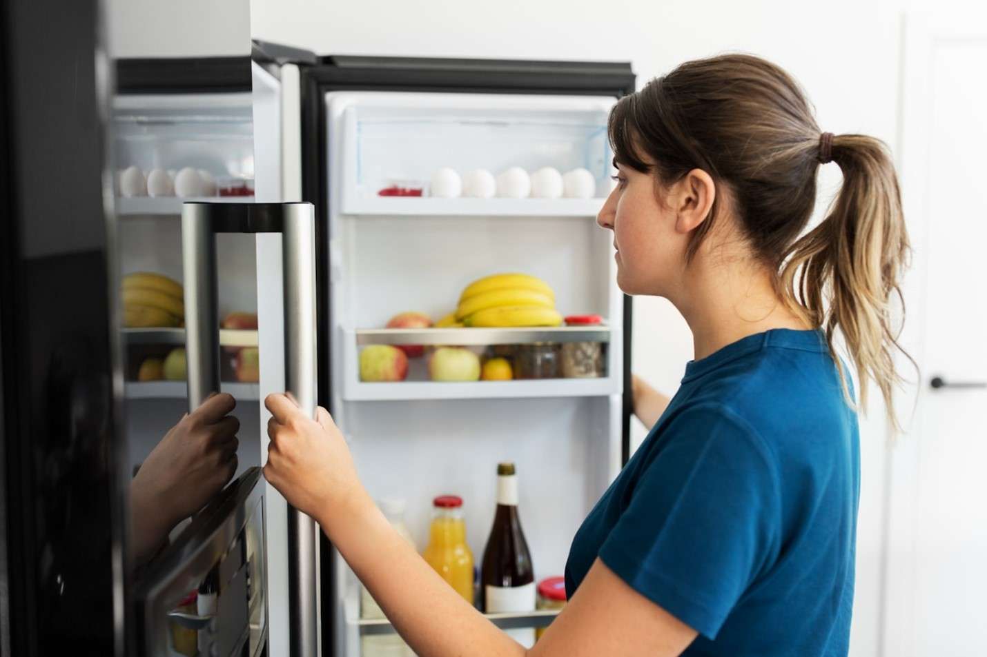 Person opening fridge with drinks, eggs, and fruits on door shelves